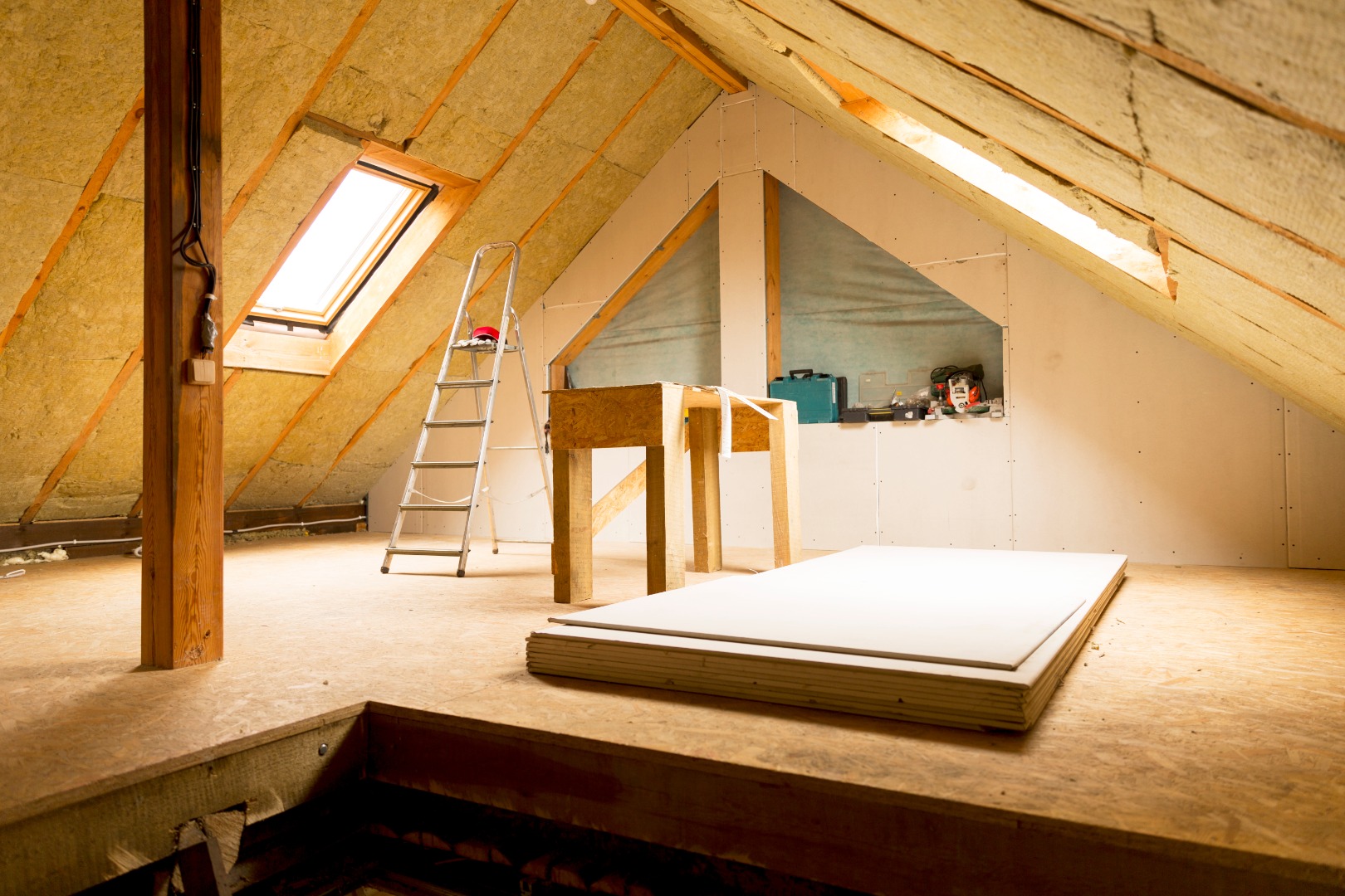 Travaux d'isolation et d'aménagement des combles, pose de laine minérale sous toiture, chantier en cours avec outillage.